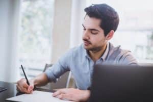 Young man taking notes in front of a computer